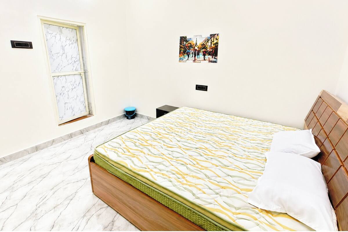 Un dormitorio con cama, un cuadro en la pared, una ventana y un cesto de basura pequeño.