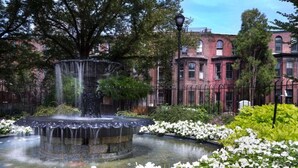 A fountain surrounded by white flowers, with a brick building in the background. - Skyline Suites on the Parkway with Full Kitchen (Philadelphia)