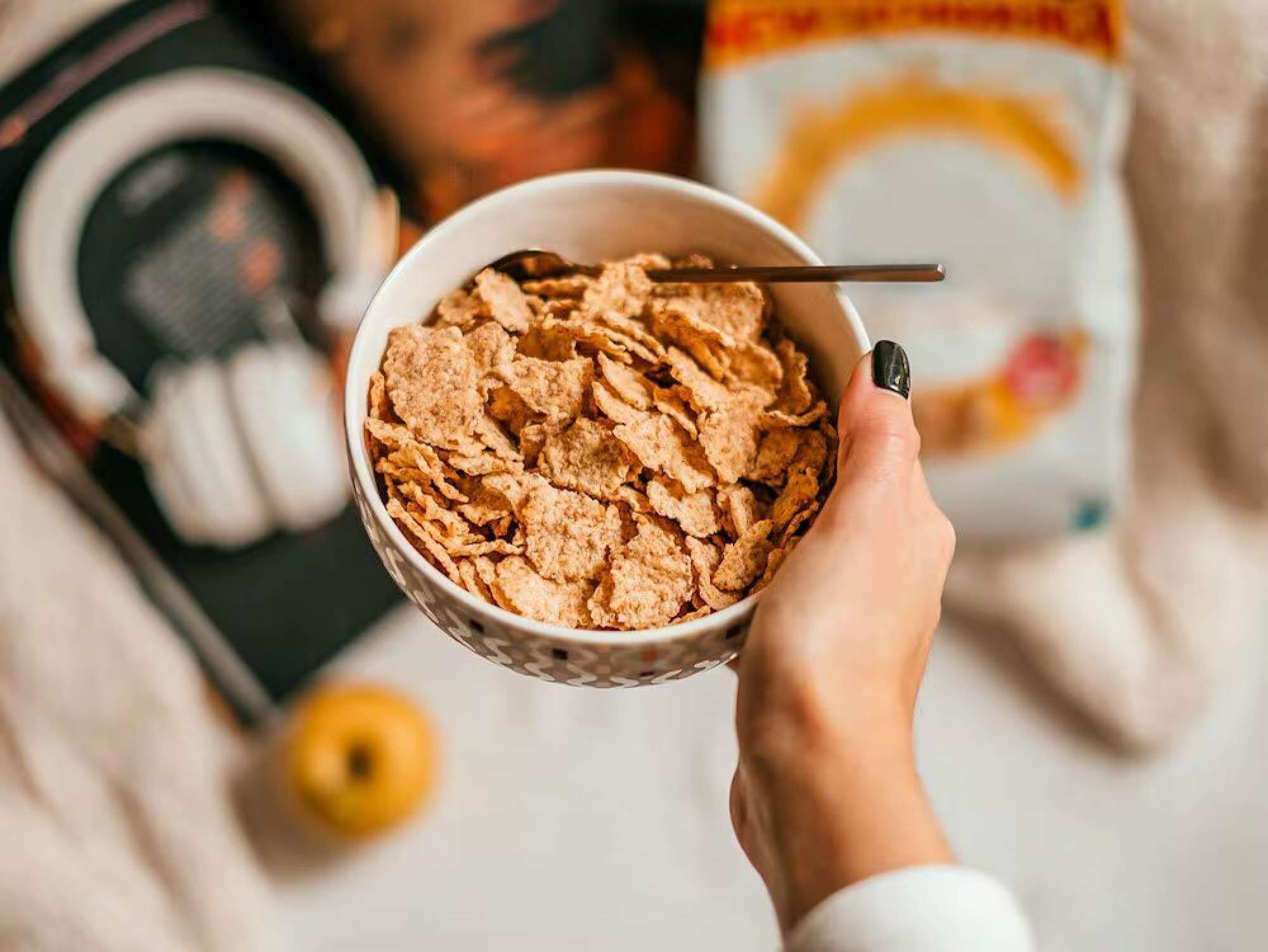 A bowl of cereal with a spoon, held by a hand.