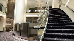 Een moderne hotel lobby met een statige trap, een receptiebalie en een decoratieve kroonluchter.