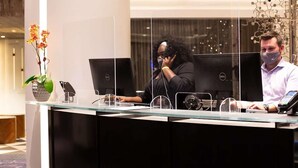 Een receptiebalie met computers, een vaas met bloemen en een decoratief metalen beeldhouwwerk.