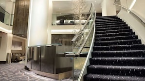 A modern hotel lobby with a grand staircase, a reception desk, and a decorative chandelier. - Near Liberty Bell | Rooftop Views + Full Kitchens (Philadelphia)