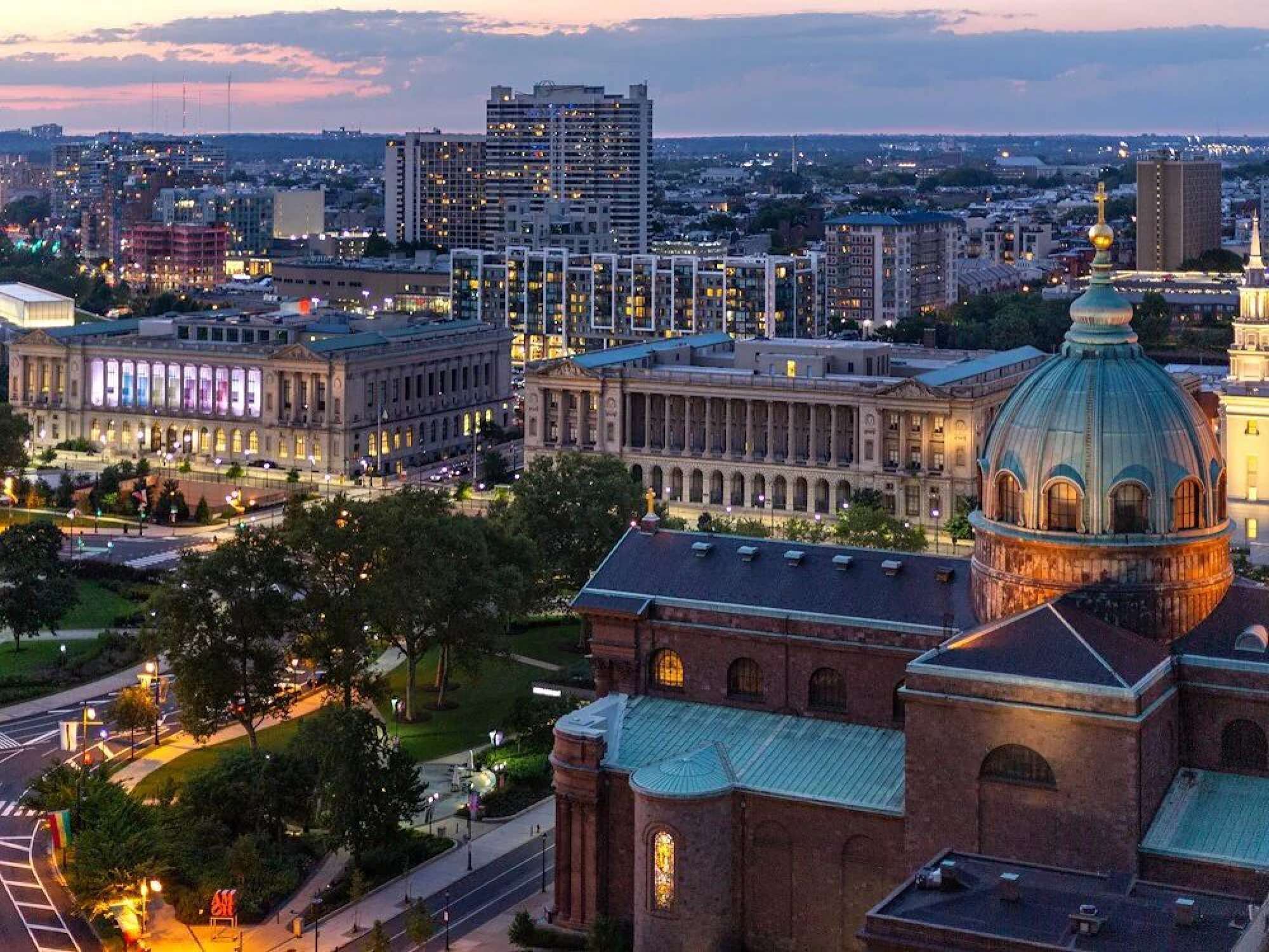 A cityscape with historic buildings, including a prominent dome structure and a large building with illuminated windows.