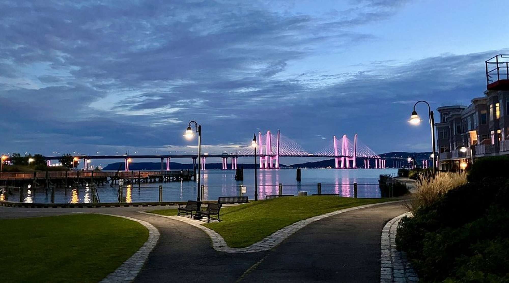 A waterfront view with a bridge, a pathway, and a building with a balcony.