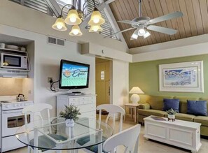 Cozinha moderna com micro-ondas, mesa de jantar com cadeiras, ventoinha no teto e uma televisão exibindo 'Epic Vacations'.