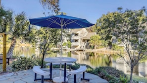 Une terrasse avec une table et des bancs, un parasol bleu et une vue sur un bâtiment situé de l’autre côté d’un lac.