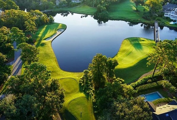 Vue aérienne d’un terrain de golf avec un étang, entouré d’arbres et d’un quartier résidentiel.