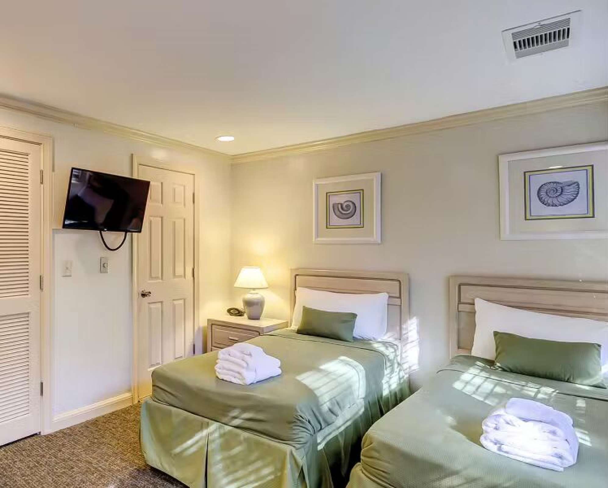 Ein Hotelzimmer mit zwei Betten, einem Fernseher, einer Lampe und Kunstwerken an den Wänden.