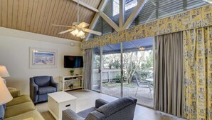 A living room with a ceiling fan, a television, and a large sliding glass door leading to an outdoor area. - Near the Beach with Pool, Hot Tub & Full Kitchen (Hilton Head)