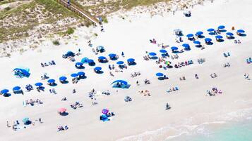 A beach with numerous blue umbrellas and people relaxing.