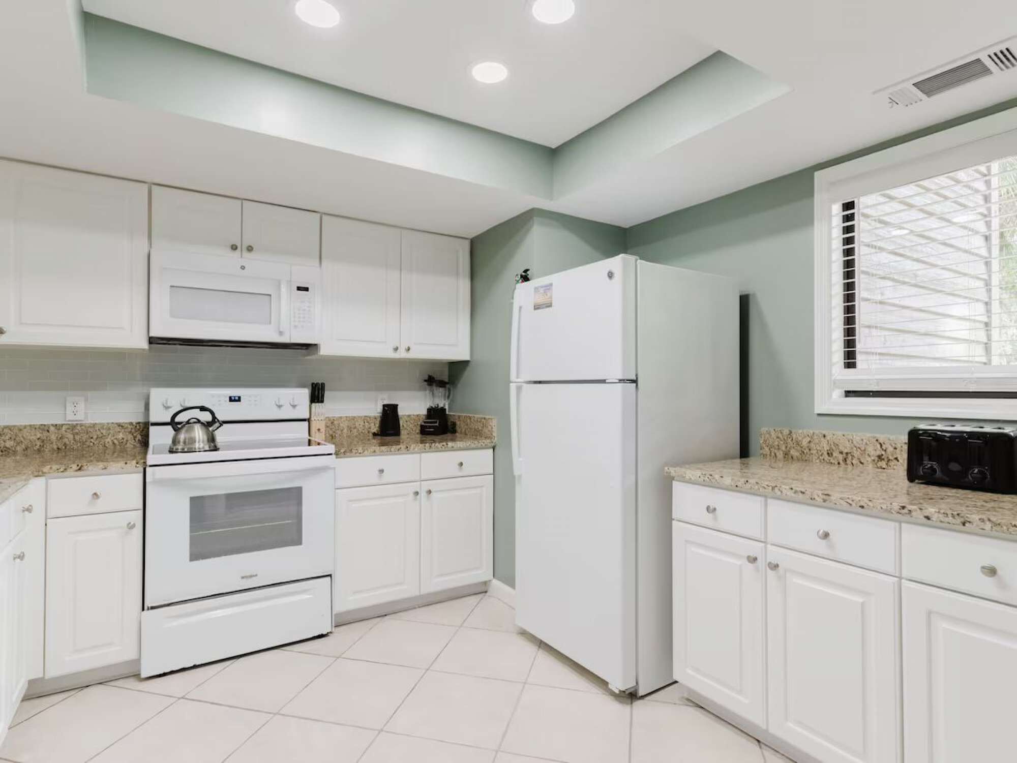 A modern kitchen with white cabinets, a microwave, a stove, and a refrigerator.