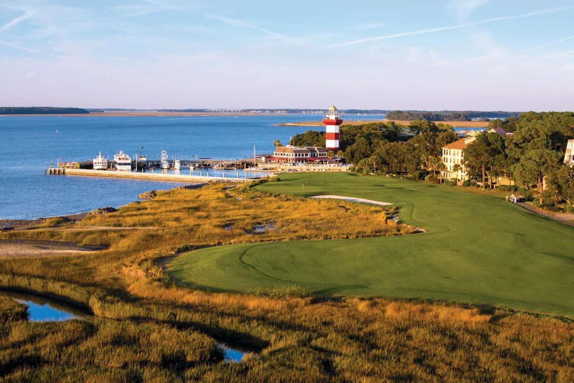 A coastal golf course with a lighthouse, a marina, and residential buildings.