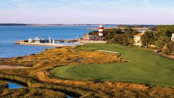 A coastal golf course with a lighthouse, a marina, and residential buildings.