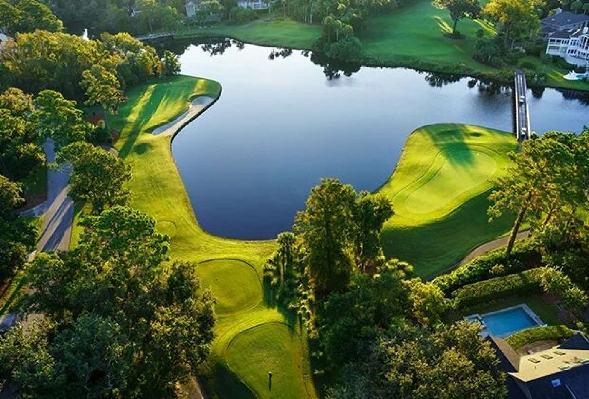 An aerial view of a golf course with a pond, surrounded by trees and a residential area.