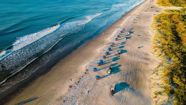 An aerial view of a beach with rows of umbrellas and beach chairs, a sandy shoreline, and the ocean. - Near the Beach | 3 Pools + Hot Tub & Full Kitchen (Hilton Head Island)