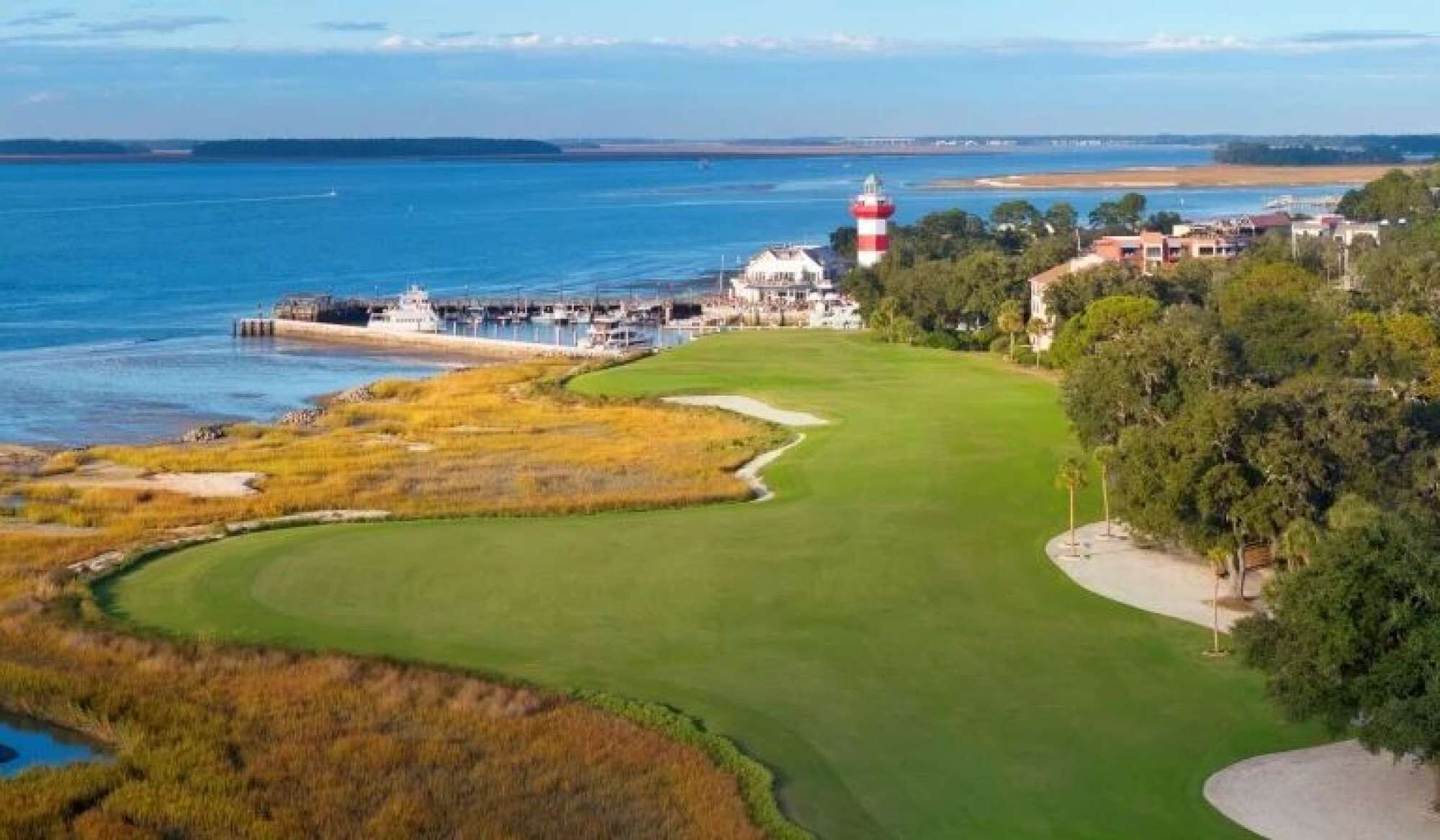 A coastal golf course with a lighthouse, water, and buildings.