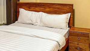 A bed with white bedding, a wooden headboard, a nightstand with drawers, and a wardrobe. - WYNE'S HOTEL STANDARD ROOM (Mbale)