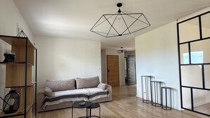 Tilava olohuone, jossa on puulattia, sohva, sohvapöytä ja geometrisesti muotoiltu kattovalaisin.