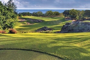 Ein Golfplatz mit Blick auf das Meer, umgeben von Bäumen und felsigem Gelände.