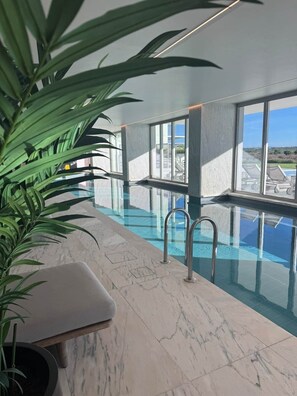 An indoor swimming pool with clear glass walls, a marble floor, and a view of the landscape outside. - The Dr Pure Spa - Bayline Beach, Spa & Gym (Armação de Pêra)
