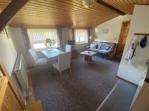 A cozy room with a wooden ceiling, a sofa, a table with chairs, a TV, and a window with curtains. - Cozy vacation apartment (2-3 persons) (Ahrenshoop)