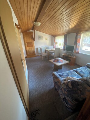A cozy room with a wooden ceiling, a sofa, a TV, and a dining table. - Cozy vacation apartment (2-3 persons) (Ahrenshoop)