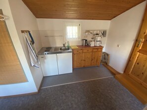 A compact kitchen with a stove, sink, wooden cabinets, and a window. - Cozy vacation apartment (2-3 persons) (Ahrenshoop)
