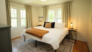 Une chambre à coucher avec un grand lit, deux tables de chevet, une commode, un tapis et un luminaire au plafond.
