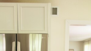 Un réfrigérateur en acier inoxydable dans une cuisine au plancher en bois, et un salon avec un canapé et un tableau accroché au mur.