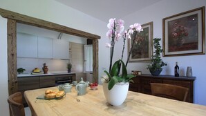 Ein Essbereich mit einem Holztisch, Stühlen, einer Vase mit Blumen und Küchenschränken im Hintergrund.