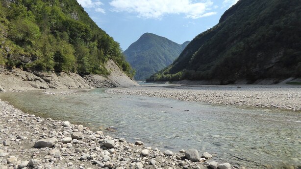 Ein Fluss mit klarem Wasser, umgeben von felsigem Gelände und grüner Vegetation.