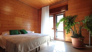 Ein Zimmer mit Holzwandverkleidung, einem Bett, einem großen Fenster und einer Zimmerpflanze.