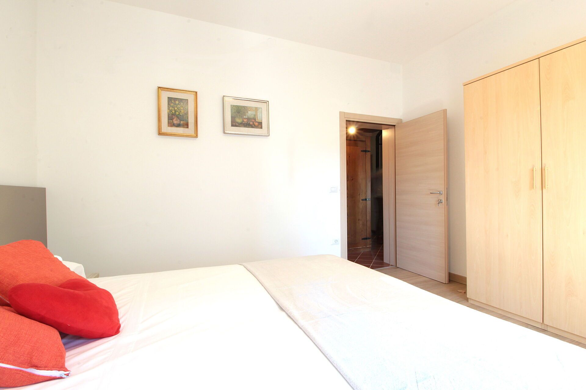 Ein Schlafzimmer mit einem Bett, zwei gerahmten Bildern, einem Kleiderschrank und einer Tür zu einem anderen Raum.