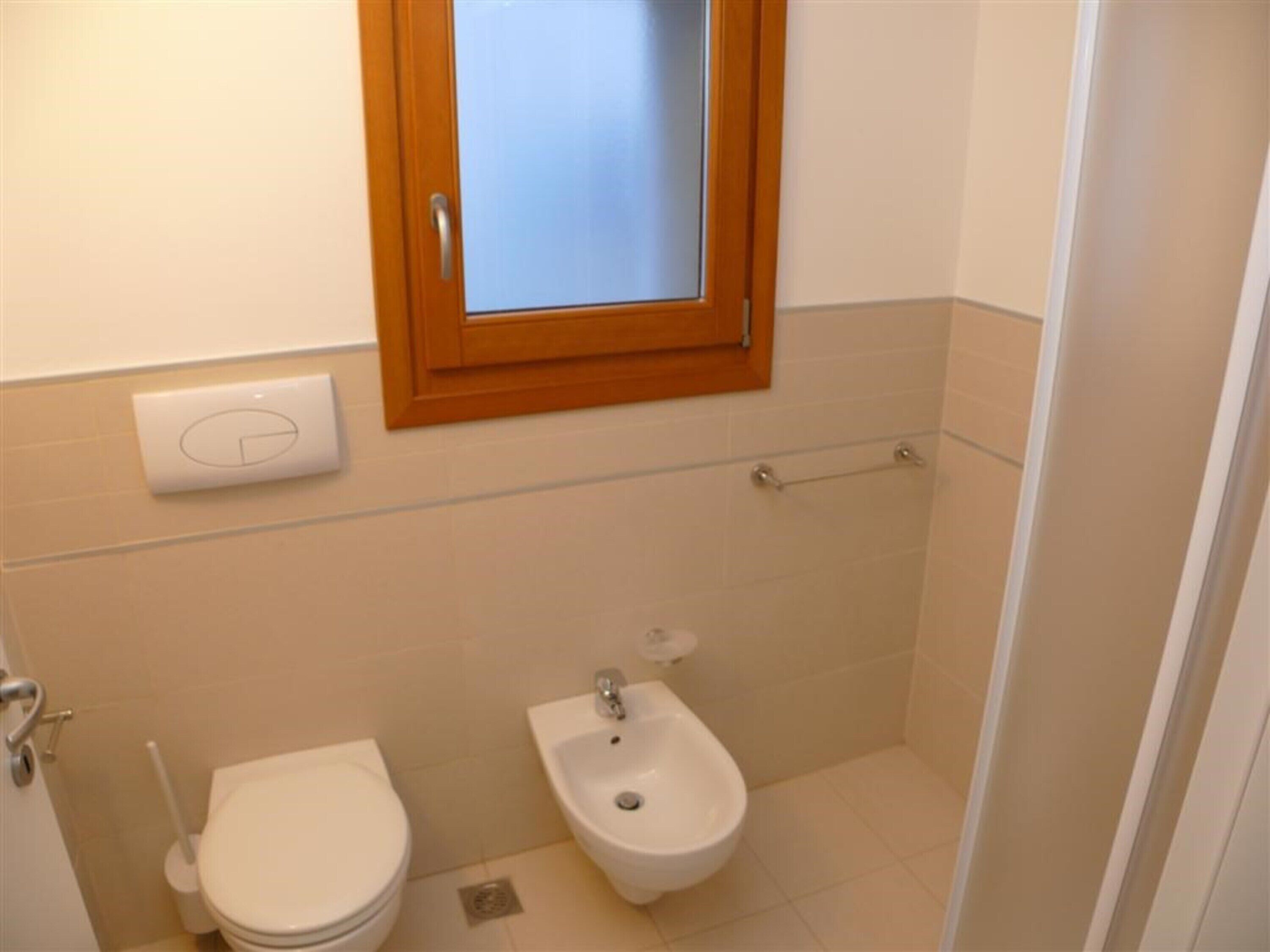 A small bathroom with a toilet, bidet, and a window above the toilet.