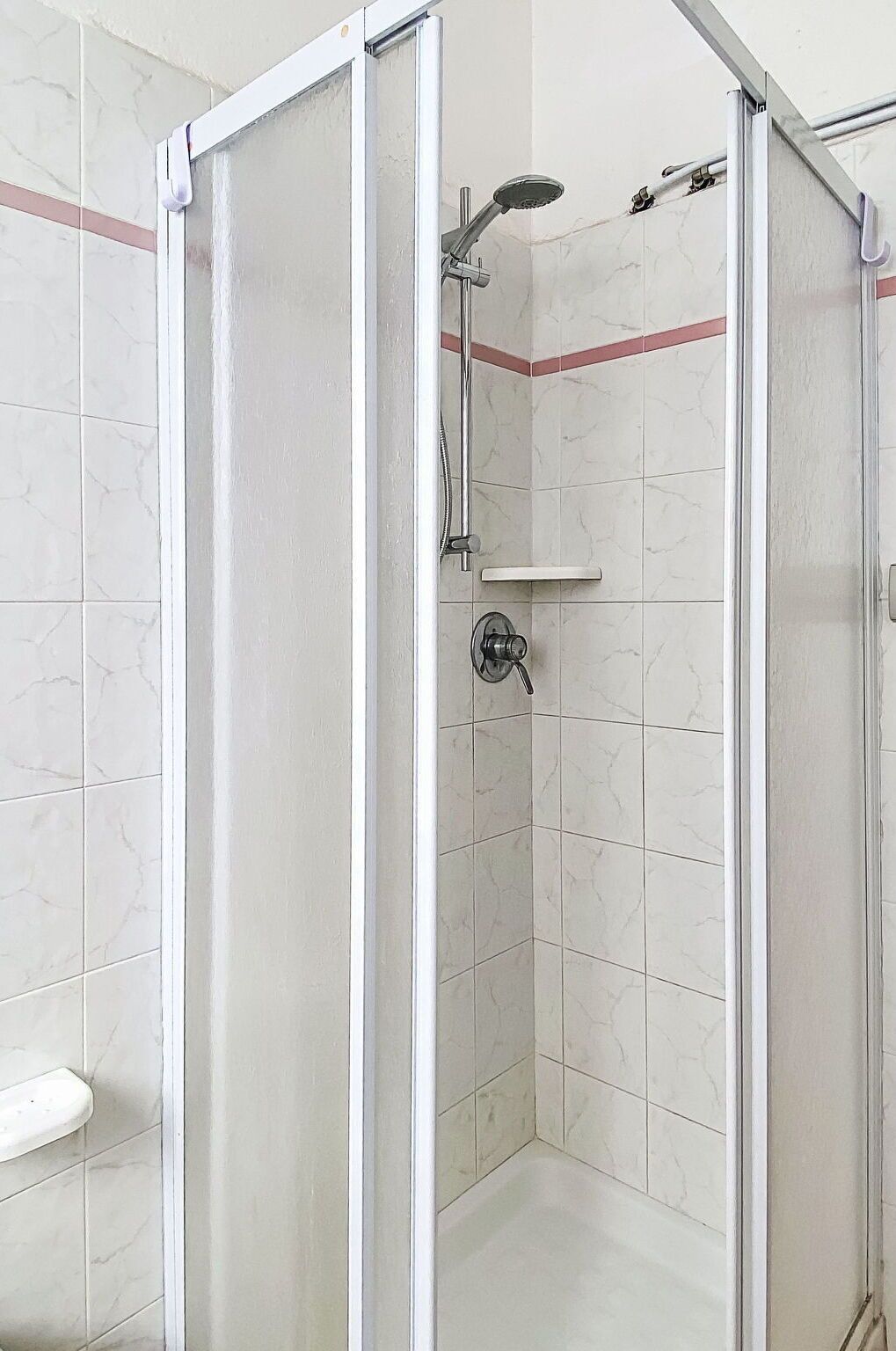 Une cabine de douche dotée d’une porte en verre, d’un pommeau de douche à main et d’un robinet mural.