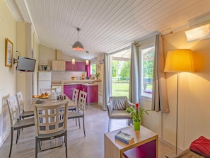 A modern kitchen with a dining area, a living space with a sofa and a table, and a view of the outdoors. - Serene Cottage Near Lot River (Castelmoron-sur-Lot)