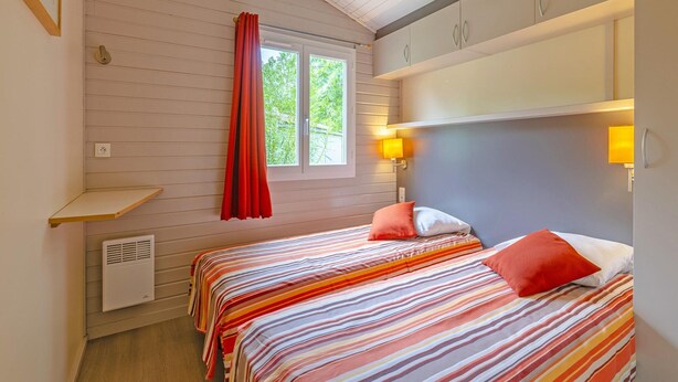 A bedroom with two beds, a window with curtains, a shelf, and a wall-mounted heater. - Serene Cottage Near Lot River (Castelmoron-sur-Lot)