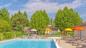 A swimming pool with lounge chairs and umbrellas, surrounded by trees and buildings. - Serene Cottage Near Lot River (Castelmoron-sur-Lot)