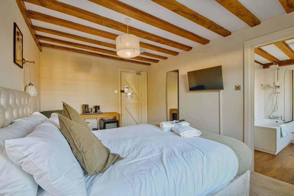 Quarto com cama, mesa de cabeceira, luminária e banheiro com banheira e chuveiro.