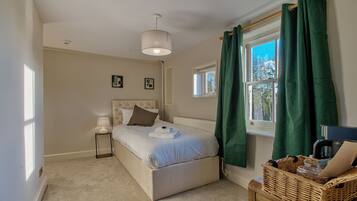 A bedroom with a bed, a nightstand, a lamp, a window with curtains, and a view of trees outside.