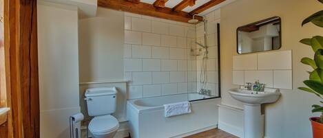 A bathroom with a toilet, bathtub, sink, wooden beams, and a mirror.