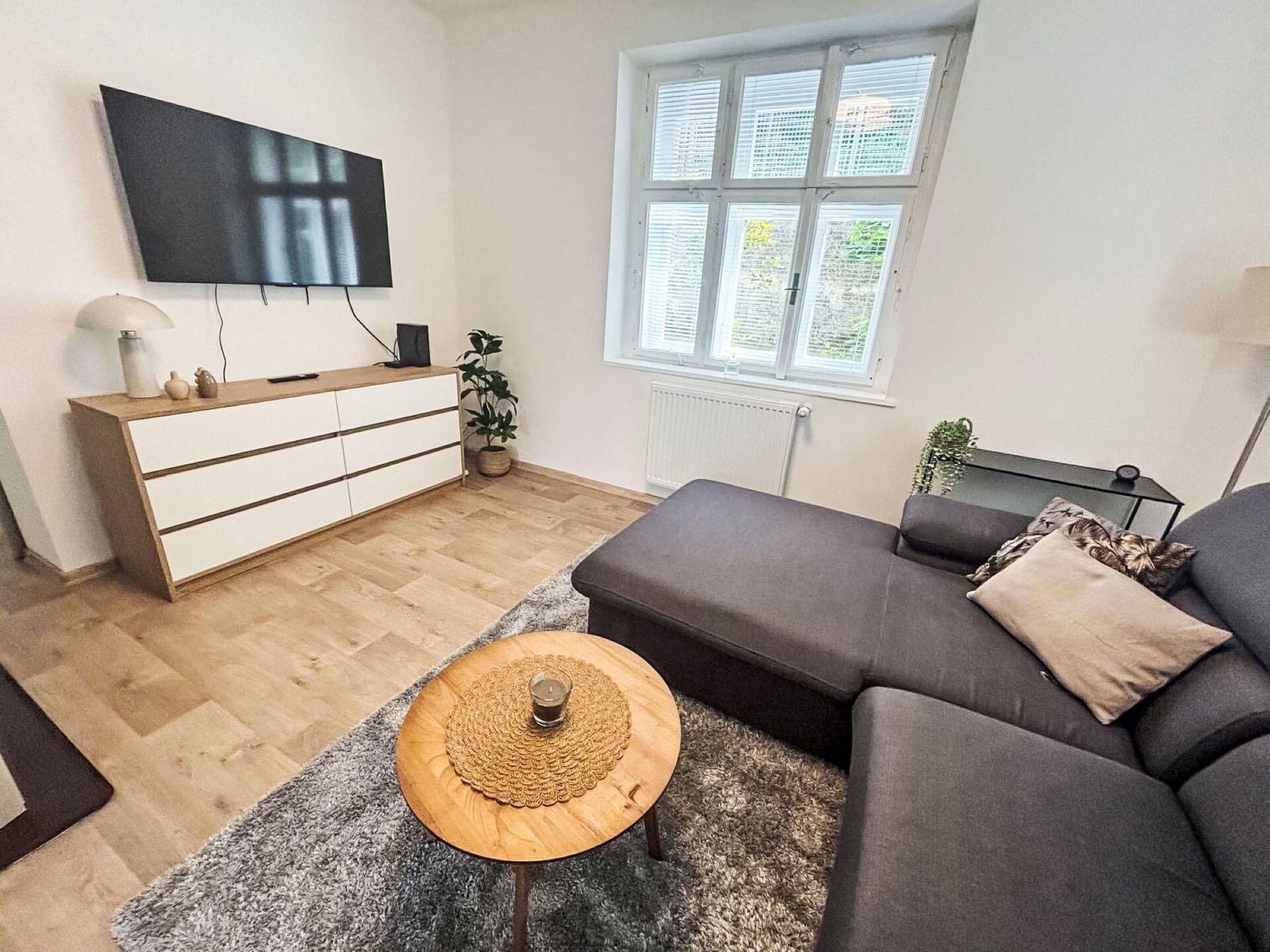 A modern living room with a sofa, a coffee table, a TV, and a window with blinds.