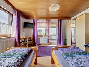 Ein Zimmer mit zwei Holzbett, einem Fernseher, einem Schreibtisch und einem Fenster mit Vorhängen.