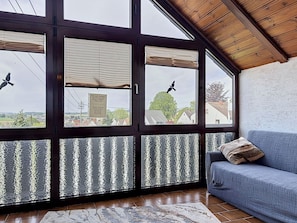 Ein Zimmer mit großen Fenstern, einem blauen Sofa und einem Fliesenboden.