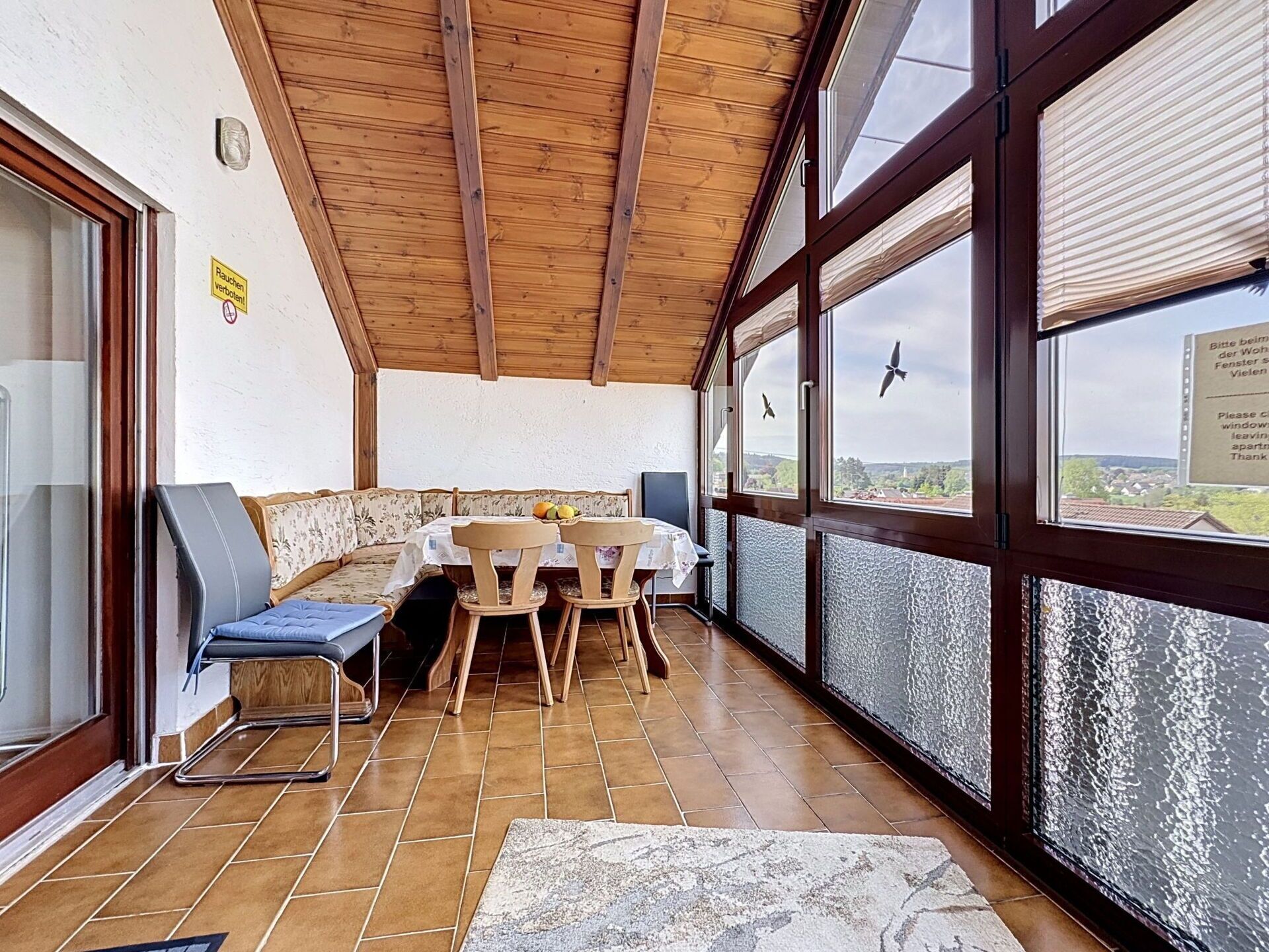 Ein Zimmer mit Holzboden, einem Tisch mit Stühlen, einer Couch und großen Fenstern mit Blick.