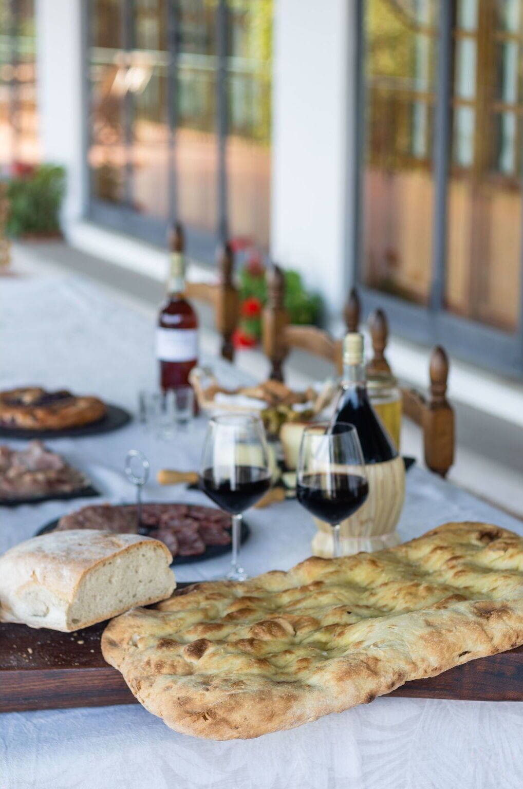 Een tafel met brood, wijn en een fles, voor een raam met uitzicht.