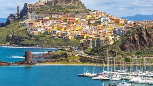 A coastal town with colorful buildings, a prominent fort on a hill, and a marina with boats. - Stunning private villa for 4 people with TV and terrace (Castelsardo)