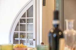 Ein Zimmer mit einer weißen Bogenförmigen Tür, einer Glasvitrine mit Geschirr und einer Flasche auf dem Tisch.