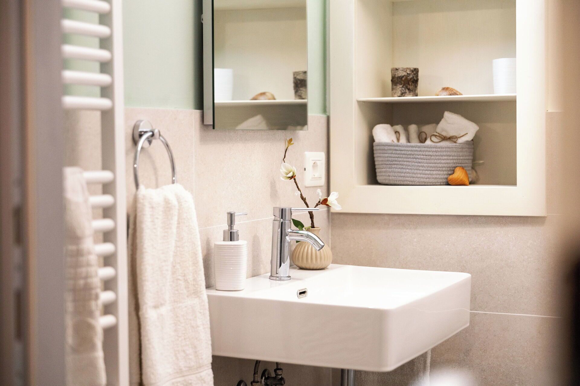 A bathroom with a white sink, a towel hanging on a rack, a mirror, and a shelf with toiletries.