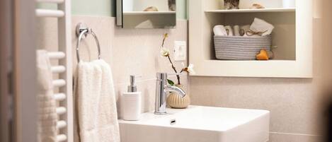 A bathroom with a white sink, a towel hanging on a rack, a mirror, and a shelf with toiletries.